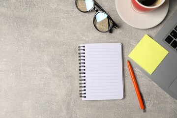 Notebook, pen, sticky note, glasses, coffee and laptop on grey table, flat lay. Space for text