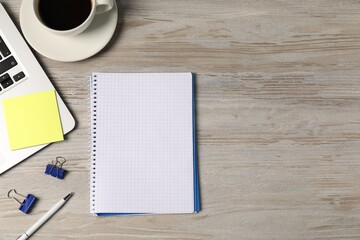 Notebook, pen, sticky note, binder clips, coffee and laptop on wooden table, flat lay. Space for text