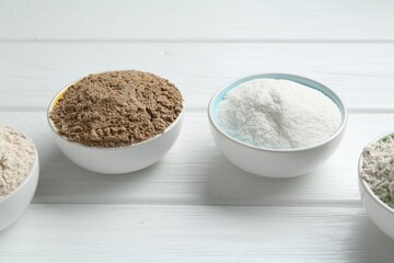 Different types of flour in bowls on white wooden table, closeup