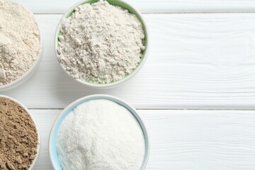 Different types of flour in bowls on white wooden table, flat lay. Space for text