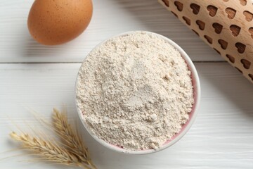 Flour in bowl, rolling pin, egg and spikes on white wooden table, flat lay