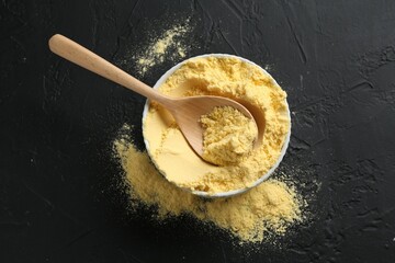 Corn flour in bowl and spoon on black textured table, top view