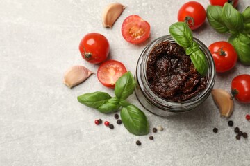 Delicious sun dried tomatoes, fresh vegetables, basil and garlic on light grey table, flat lay