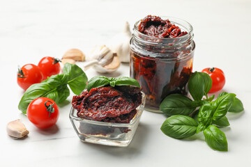 Delicious sun dried tomatoes, fresh vegetables, basil and garlic on white table, closeup