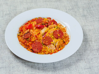 Fine tasty Spanish paella dinner with rice and high quality chorizo sausage on white plate and simple table cloth. Mediterranean style dish. Popular food made from premium ingredients.