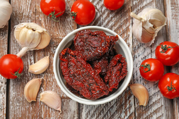 Delicious sun dried tomatoes, fresh vegetables and garlic on wooden table, flat lay