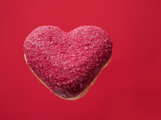 Red creative heart shaped donut floating in the air, red color saturated background. Love and romance concept. Valentine gift idea. Transforming food for marketing reasons to increase sales.