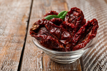 Delicious sun dried tomatoes with basil in glass bowl on wooden table, closeup. Space for text