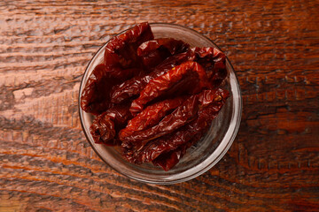 Delicious sun dried tomatoes in glass bowl on wooden table, top view