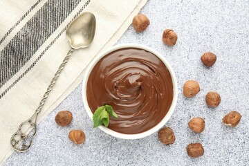 Tasty chocolate spread with mint in bowl and hazelnuts on grey textured table, flat lay