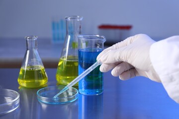 Scientist taking sample with pipette out of Petri dish at table in laboratory, closeup