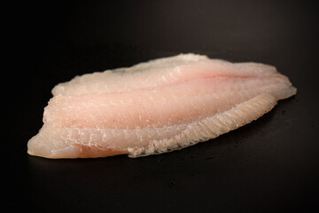 Fresh tilapia fillet on black background, top view.
