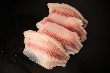 Fresh tilapia fillet on black background, top view.