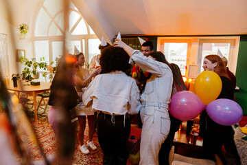 Group of nine friends standing and putting on birthday hats while laughing