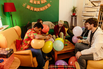 Group of five friends sitting at a table and blowing up balloons, at a party