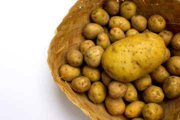 A large potato and several small potatoes in a basket made of woven bamboo, isolated on white.