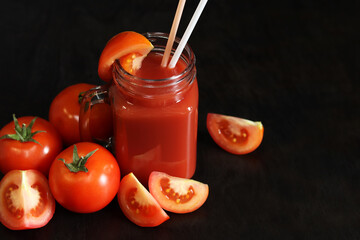 Tomato juice on a dark background. Vegetable diet drink. Fresh tomato juice in a glass with a handle. Ripe red tomatoes and juice made from them. Glass with juice and a straw, tomatoes. Healthy drink