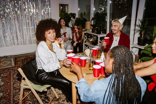 A group of four friends sit at a table and laugh while talking and clinking cups