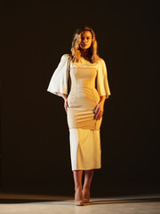 Girl model in beige dress on black studio background.