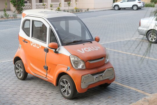 Orange and white Valu-branded electric microcar parked on a paved lot in El Gouna, Red Sea Governorate, Egypt. May 3, 2025. The compact, two-door vehicle features distinctive styling with a small fram