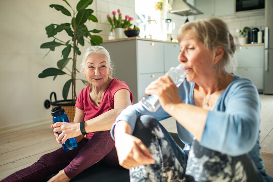 Senior lesbian couple drinking water out of a reusable bottle while exercising and working out at home