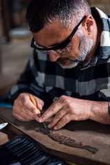 Carpenter sitting in his workshop restoring old piece of furniture with carving tool.