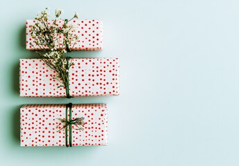 Three small gift boxes, stacked vertically, are wrapped in white paper with red polka dots.  Small sprigs of white flowers are tied with light green twine around each gift