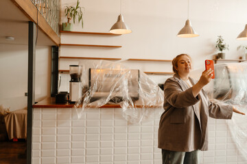 A female owner stands and talks while looking at a phone she holds in front of her, in a cafe