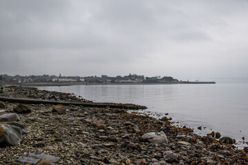 view up coastline to Victorian town Dunoon in Scotland, rocky beach leads into Firth of Clyde calm water coastline on grey cloudy day