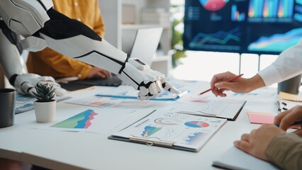 A robotic arm collaborates with humans in a modern office, analyzing data through charts and graphs, showcasing the integration of technology in business strategies.Noogenesis