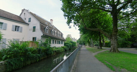 Scenic pathway along a serene canal with trees and greenery on both sides, leading past a charming house, inviting viewers to explore the tranquil beauty of this natural landscape