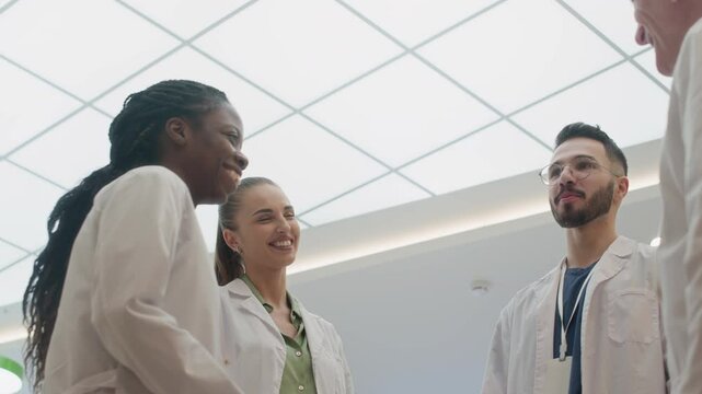 Low angle shot of multiethnic team of medical professionals all smiling and chatting amicably during break while standing in clinic corridor