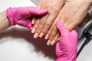 French Manicure Finish at Beauty Salon, Close-up of freshly done French manicure with pink and white tips, held by gloved hands.
