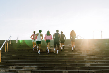 A group of six athletes are running up the stairs, outdoors