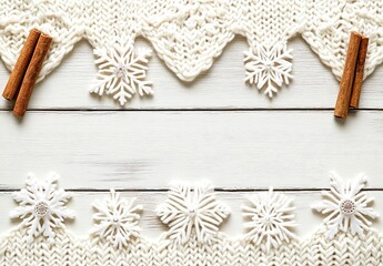 White knitted fabric border with snowflakes and cinnamon sticks on a light wooden background