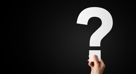 A hand holding a large white question mark against a plain black background in a studio setting real estate business ,technology ,selling ,purchasing ,agreement