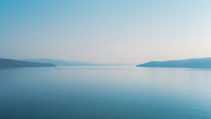 Aerial perspective of a vast lake nestled among green hills and rugged mountains under a bright blue sky