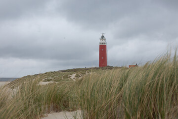 The Eierland Lighthouse on the northernmost top of the Dutch island of Texel, Red lighthouse tower on the sand dunes with european marram grass and cloudy sky as background, North Holland, Netherlands