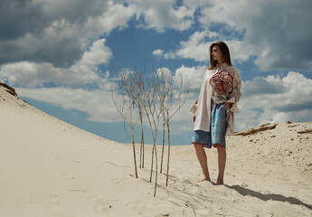 Fashion shooting in the desert, girl model in a beige shirt and blue shorts.