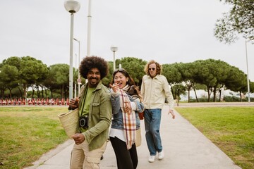 Obraz premium A man holds a bag while looking in the direction pointed by his female friend who is walking next to him and holding a dog, they are laughing, outdoors