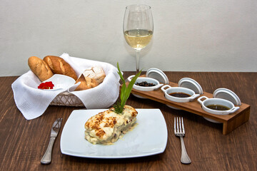 Fish dish with melted cheese accompanied by sauce and glass of white wine on restaurant table
