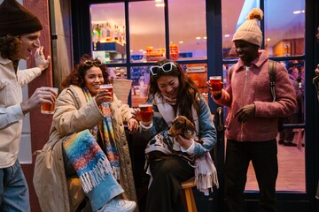 Group of five friends laughing and holding a glass while one of them holds a dog, outdoors
