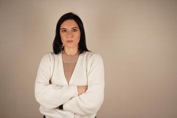 Portrait of sad depressed cute brunette woman folding arms, frowning, wearing white sweater isolated standing on peach background in studio.