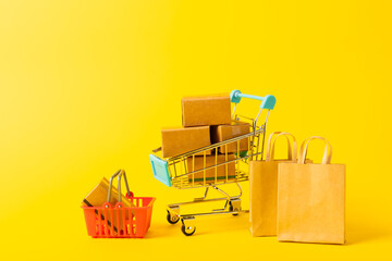 Online shopping concept.Cardboard box and shopping bags in a trolley on a bright colored background. Shopping basket. Online shopping using a laptop, tablet, phone and credit card. Home delivery.