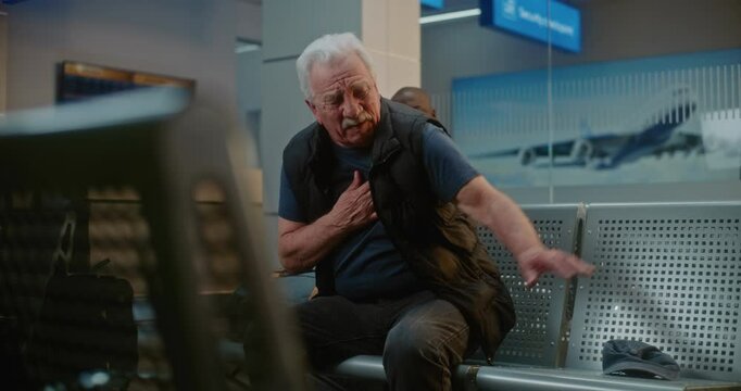 Crowded International Airport Terminal: Senior Man Having Heart Attack, Clutching Chest in Pain Sitting in Departure Lounge of Airline Hub. Diverse People and Airport Staff Helping Elderly Passenger.
