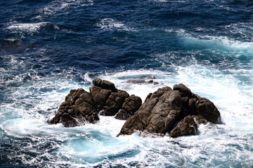 Foamy turquoise waves crashing on rugged coastal rocks in the deep blue sea