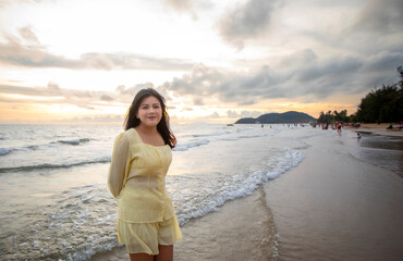 Beautiful Asian woman walking peacefully on a desert beach during sunset, with freedom concept, with amazing orange sky and sunlight reflecting on the sea and sand.