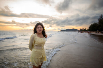 Beautiful Asian woman walking peacefully on a desert beach during sunset, with freedom concept, with amazing orange sky and sunlight reflecting on the sea and sand.
