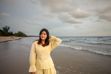 Beautiful Asian woman walking peacefully on a desert beach during sunset, with freedom concept, with amazing orange sky and sunlight reflecting on the sea and sand.