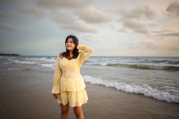 Beautiful Asian woman walking peacefully on a desert beach during sunset, with freedom concept, with amazing orange sky and sunlight reflecting on the sea and sand.
